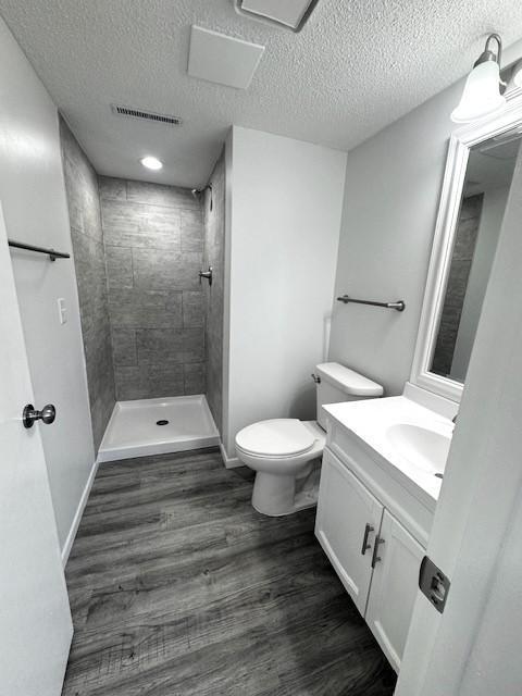 bathroom with toilet, a textured ceiling, a tile shower, vanity, and hardwood / wood-style floors