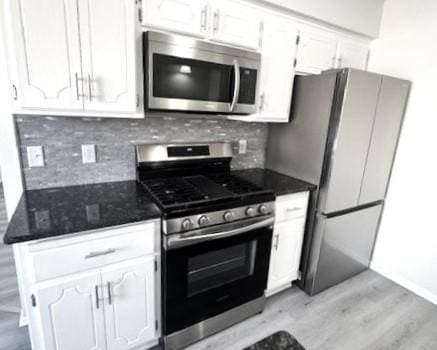 kitchen with stainless steel appliances, white cabinetry, backsplash, and light hardwood / wood-style flooring