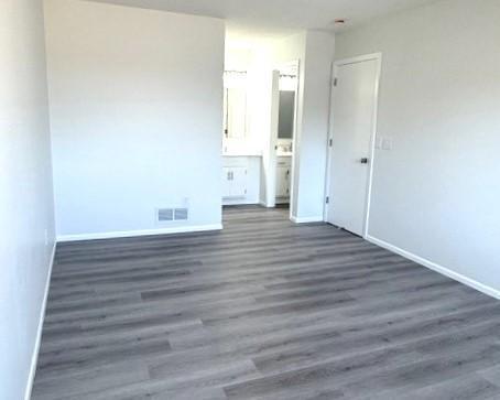 unfurnished bedroom featuring ensuite bathroom and dark hardwood / wood-style flooring