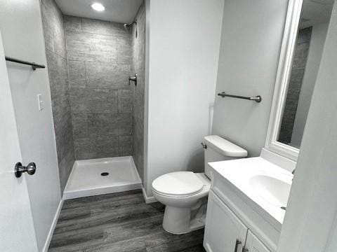 bathroom with hardwood / wood-style flooring, vanity, tiled shower, and toilet