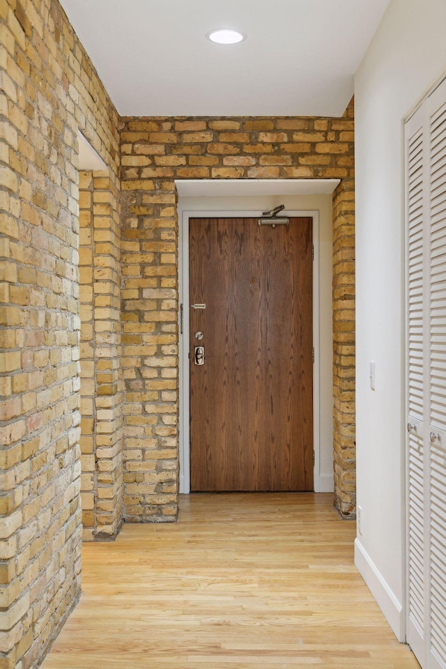 hallway with brick wall and light hardwood / wood-style flooring