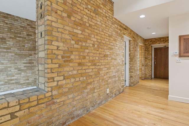 hall with brick wall and light wood-type flooring