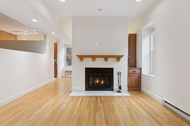 unfurnished living room featuring a baseboard radiator, track lighting, and light wood-type flooring