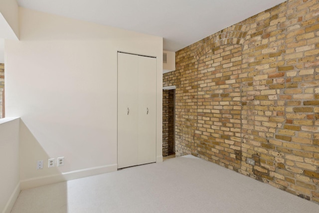 unfurnished bedroom featuring light colored carpet, a closet, and brick wall