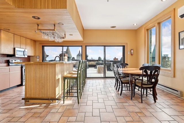 kitchen with appliances with stainless steel finishes, a breakfast bar area, backsplash, baseboard heating, and a wall unit AC