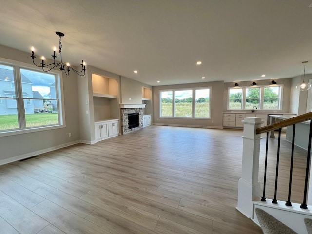 unfurnished living room featuring a chandelier, built in features, a fireplace, and light hardwood / wood-style flooring