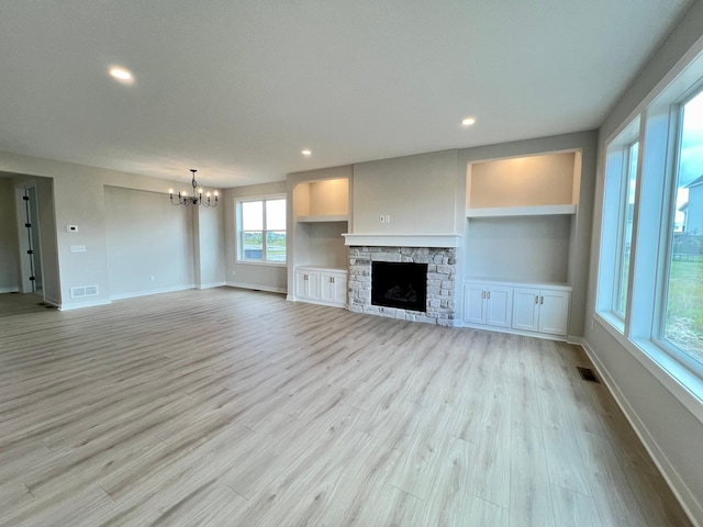 unfurnished living room featuring built in features, a stone fireplace, a notable chandelier, and light hardwood / wood-style flooring