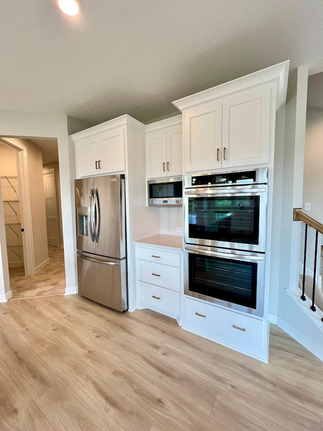 kitchen with stainless steel appliances, light hardwood / wood-style flooring, and white cabinets