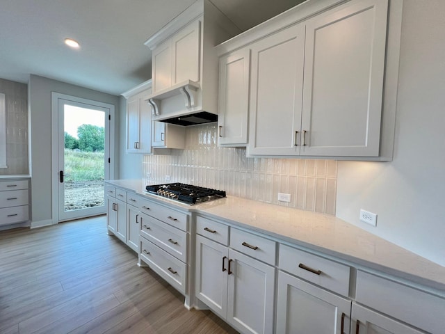 kitchen with white cabinetry, stainless steel gas cooktop, light stone counters, and decorative backsplash