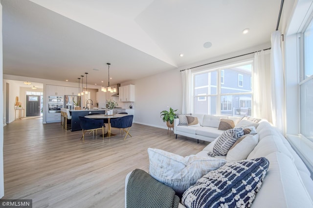 living room featuring lofted ceiling, sink, a chandelier, and light wood-type flooring