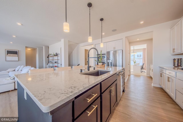 kitchen with sink, white cabinetry, a kitchen island with sink, hanging light fixtures, and stainless steel fridge with ice dispenser