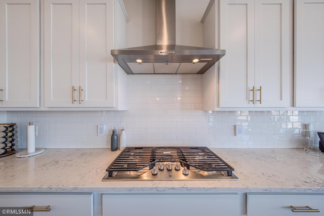 kitchen with range hood, stainless steel gas stovetop, white cabinetry, decorative backsplash, and light stone counters