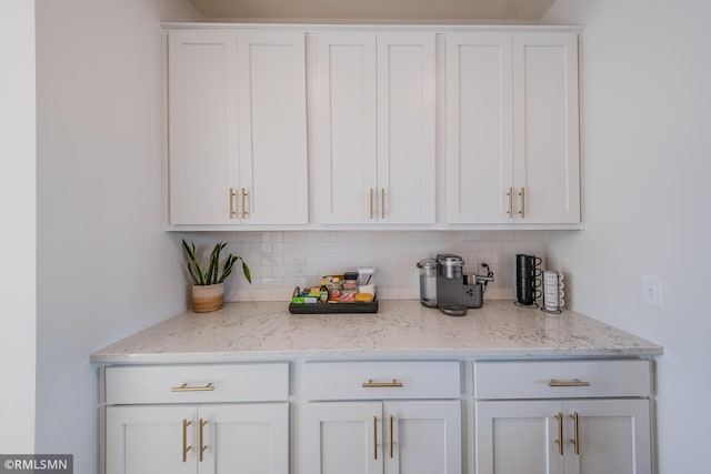 bar with light stone counters, tasteful backsplash, and white cabinets