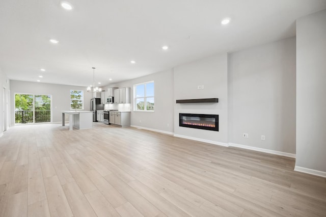 unfurnished living room with an inviting chandelier and light wood-type flooring