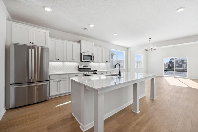 kitchen with pendant lighting, sink, stainless steel appliances, white cabinets, and a center island with sink