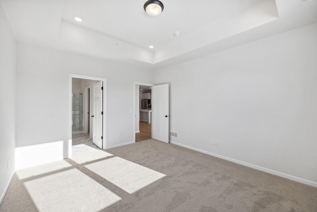 unfurnished bedroom with light carpet, ensuite bath, and a raised ceiling