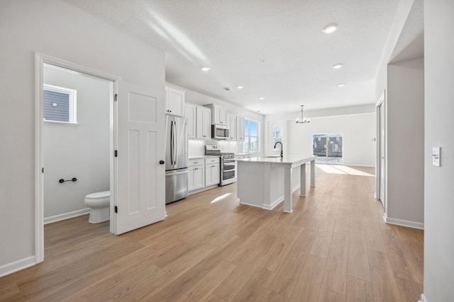 kitchen featuring decorative light fixtures, white cabinets, a kitchen island with sink, stainless steel appliances, and light wood-type flooring