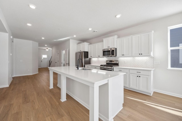 kitchen featuring stainless steel appliances, a kitchen island with sink, sink, and white cabinets