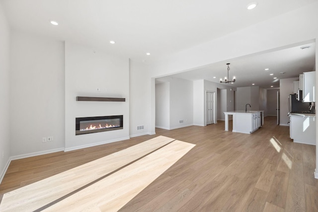 unfurnished living room with a chandelier, light hardwood / wood-style floors, and sink