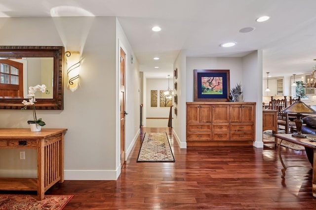 corridor with dark wood finished floors, an inviting chandelier, recessed lighting, and baseboards