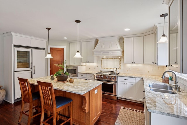 kitchen with dark wood-style floors, premium range hood, a sink, white cabinets, and built in appliances