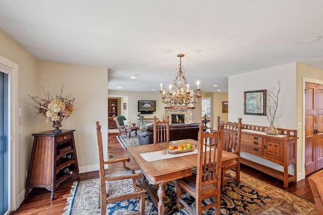 dining space featuring wood finished floors, a fireplace, a chandelier, baseboards, and recessed lighting