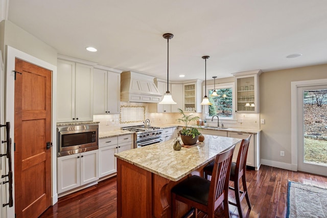 kitchen featuring custom range hood, appliances with stainless steel finishes, glass insert cabinets, tasteful backsplash, and dark wood-type flooring