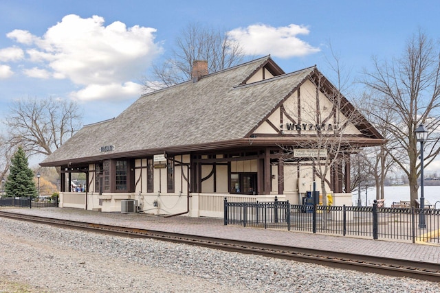 view of front facade with roof with shingles, a chimney, and central AC