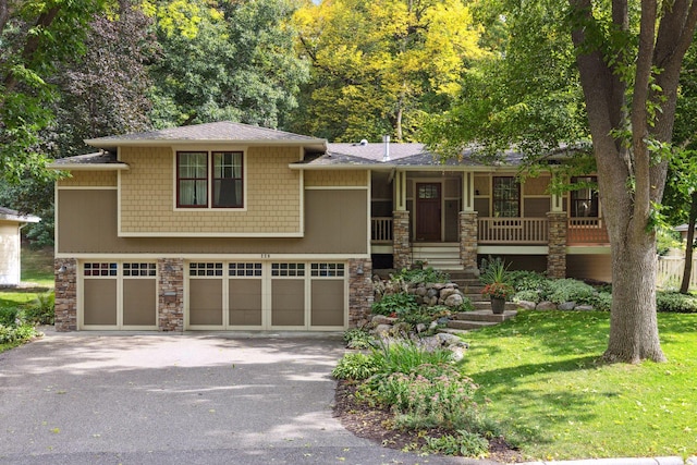 view of front of home featuring stone siding, asphalt driveway, an attached garage, and covered porch