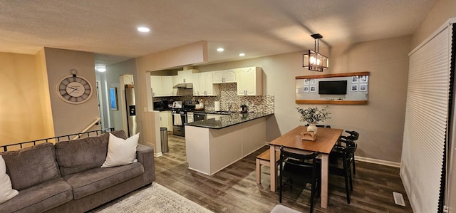 kitchen featuring appliances with stainless steel finishes, hanging light fixtures, backsplash, dark hardwood / wood-style flooring, and kitchen peninsula