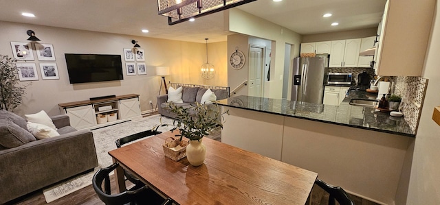 interior space with appliances with stainless steel finishes, pendant lighting, decorative backsplash, dark stone counters, and kitchen peninsula