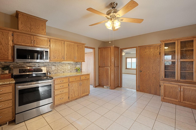 kitchen with light stone counters, light tile patterned floors, ceiling fan, stainless steel appliances, and decorative backsplash