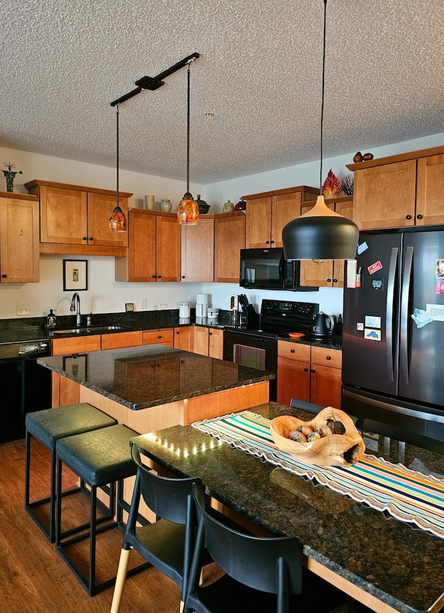 kitchen with brown cabinets, a breakfast bar, hanging light fixtures, black appliances, and a sink