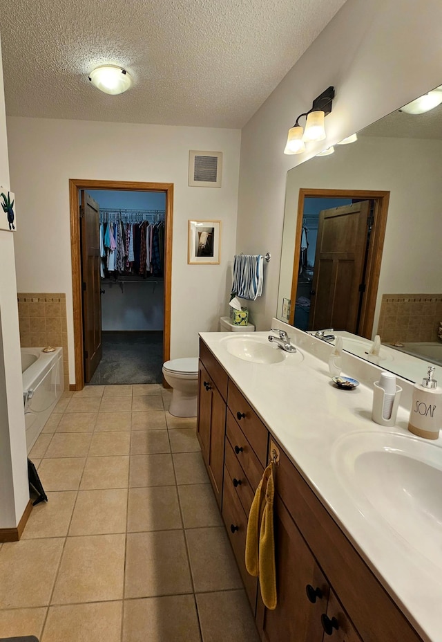 bathroom with a garden tub, a sink, a spacious closet, tile patterned floors, and double vanity