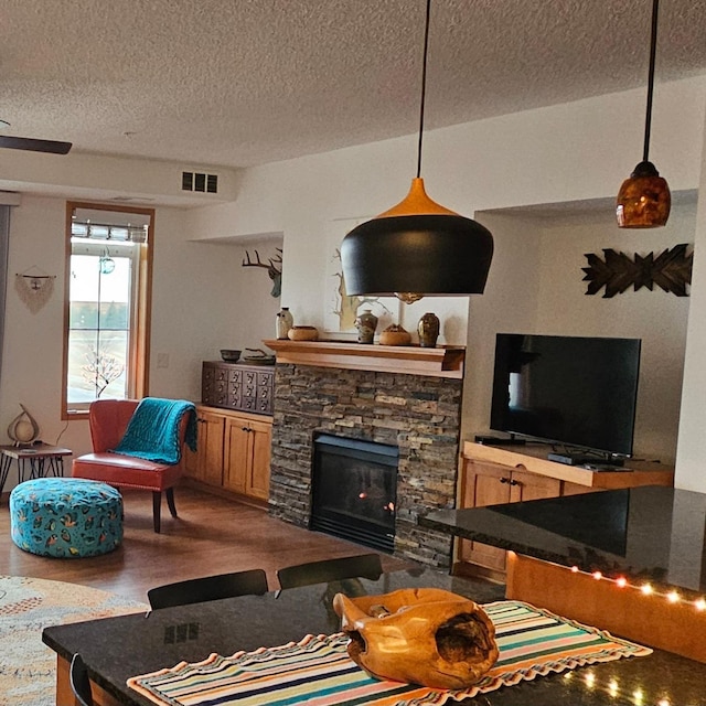 living room with a textured ceiling, a fireplace, visible vents, and wood finished floors