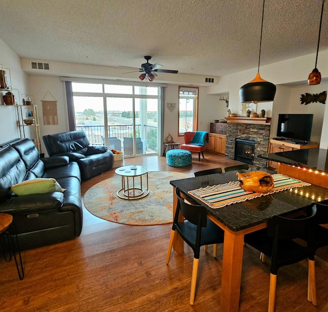 living area featuring a textured ceiling, a stone fireplace, wood finished floors, and visible vents