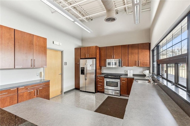 kitchen with appliances with stainless steel finishes, brown cabinets, a high ceiling, light speckled floor, and a sink