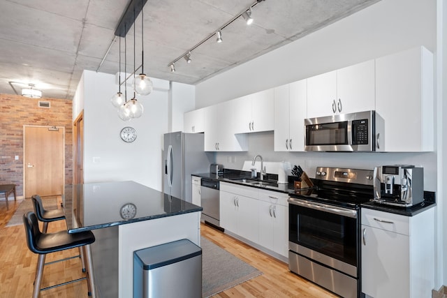 kitchen with sink, white cabinetry, decorative light fixtures, light hardwood / wood-style flooring, and stainless steel appliances