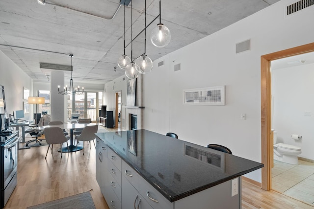 kitchen with gray cabinets, a kitchen island, pendant lighting, dark stone counters, and light hardwood / wood-style floors