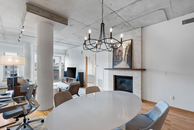 dining area with wood-type flooring, rail lighting, decorative columns, and a tile fireplace