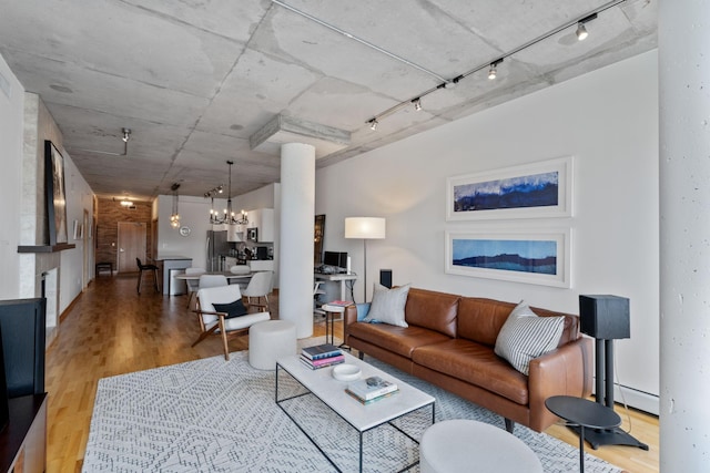 living room with a chandelier, light wood-type flooring, track lighting, decorative columns, and a baseboard heating unit