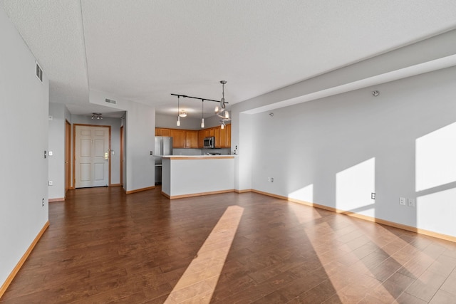 unfurnished living room with track lighting, a textured ceiling, and dark hardwood / wood-style flooring