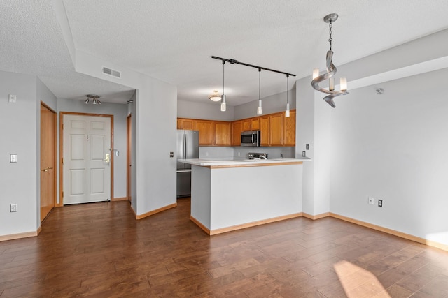 kitchen with dark wood-type flooring, stainless steel appliances, a textured ceiling, decorative light fixtures, and kitchen peninsula