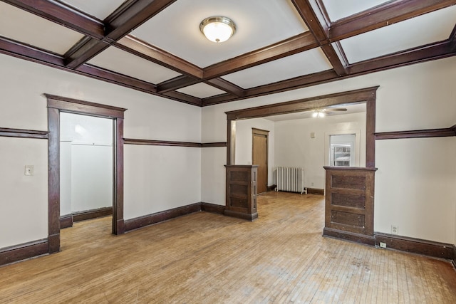 empty room with beamed ceiling, coffered ceiling, radiator, and light wood-type flooring