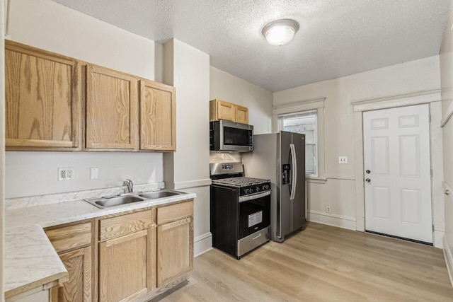 kitchen featuring appliances with stainless steel finishes, light brown cabinetry, sink, light wood-type flooring, and a textured ceiling