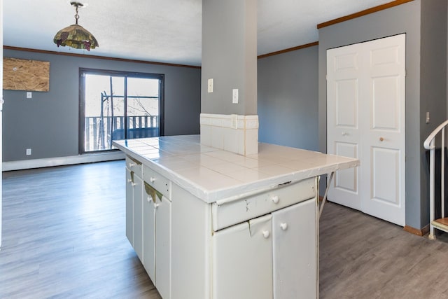 kitchen featuring hardwood / wood-style floors, tile countertops, white cabinetry, hanging light fixtures, and crown molding