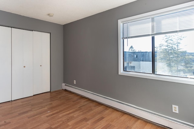 unfurnished bedroom featuring a baseboard radiator, a closet, and wood-type flooring