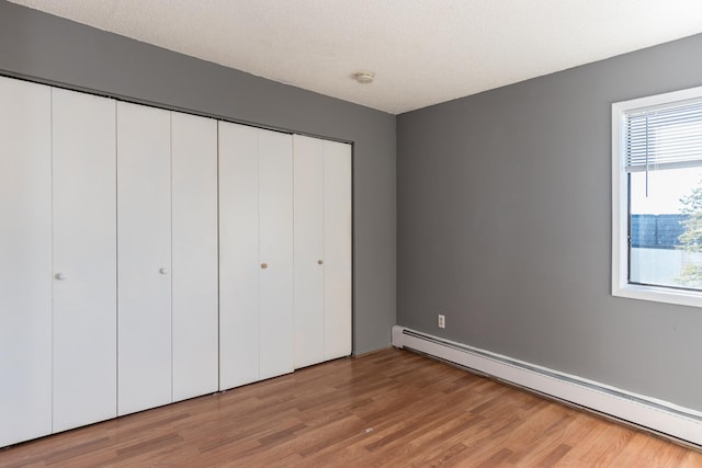 unfurnished bedroom with a textured ceiling, hardwood / wood-style floors, a closet, and a baseboard heating unit