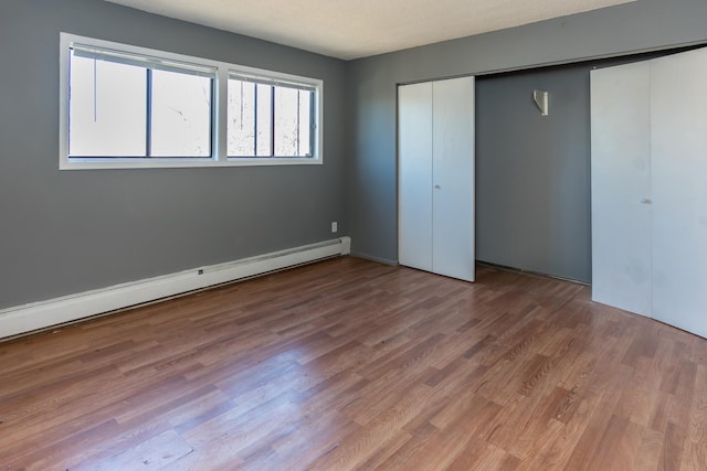 unfurnished bedroom featuring hardwood / wood-style flooring, a baseboard radiator, and a closet