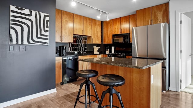 kitchen featuring dark stone countertops, a center island, light wood-type flooring, black appliances, and a kitchen bar